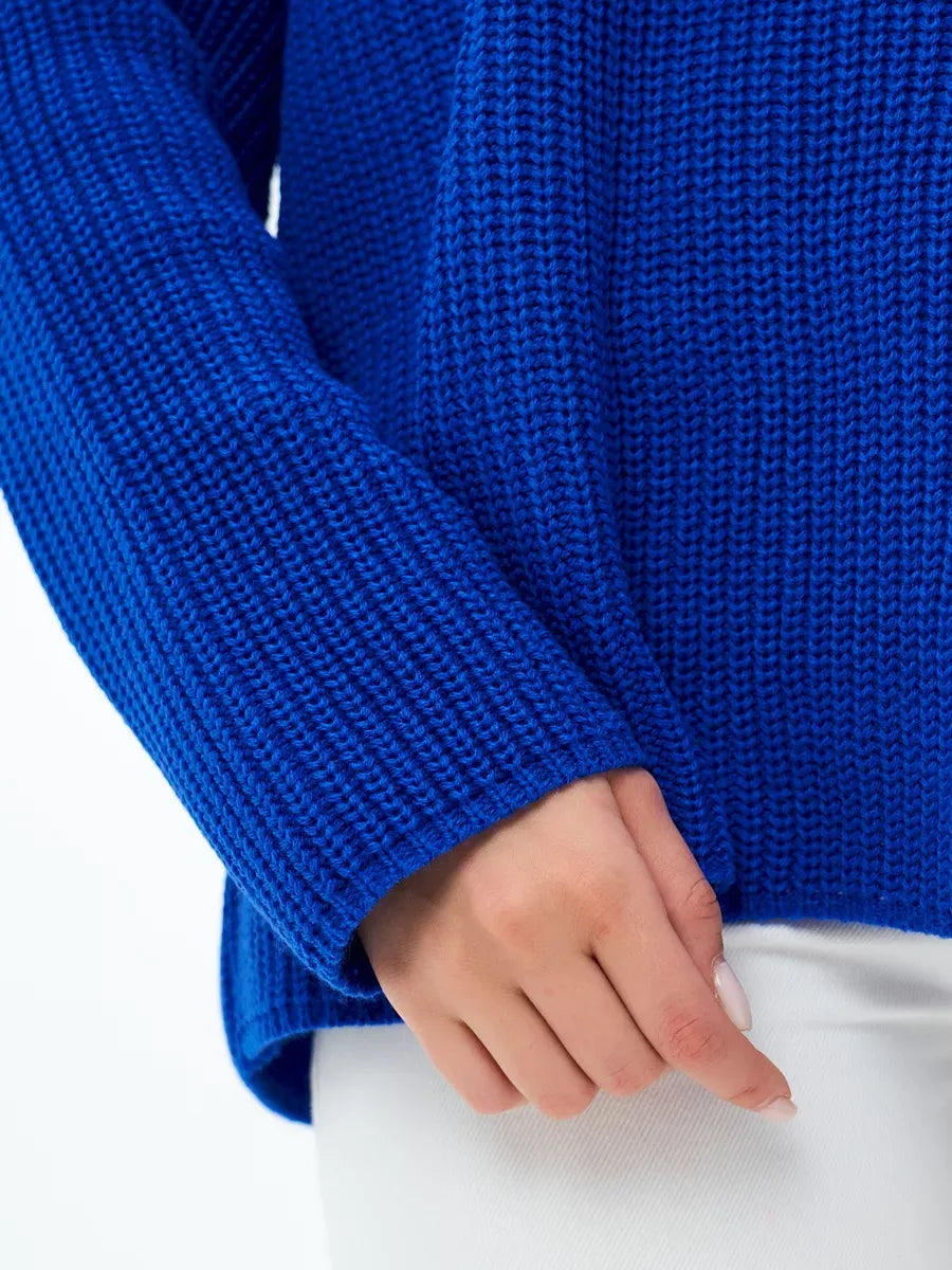 Close-up of a hand holding the sleeve of the vibrant blue Capri Sweater by Lauven, showcasing its textured knit design.