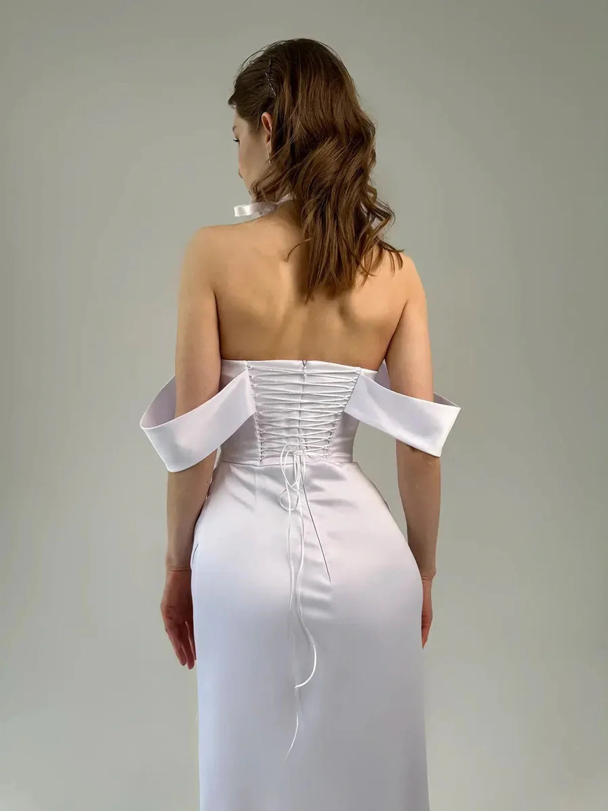 Eira Occasion Dress by Lauven; elegant white satin off-shoulder gown with draping and a high slit, showcased from the back.