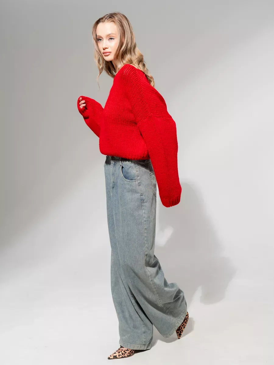 Model wearing the Scarlet Sweater by Lauven, an oversized off-shoulder knit in deep red with stylish gray wide-leg pants.