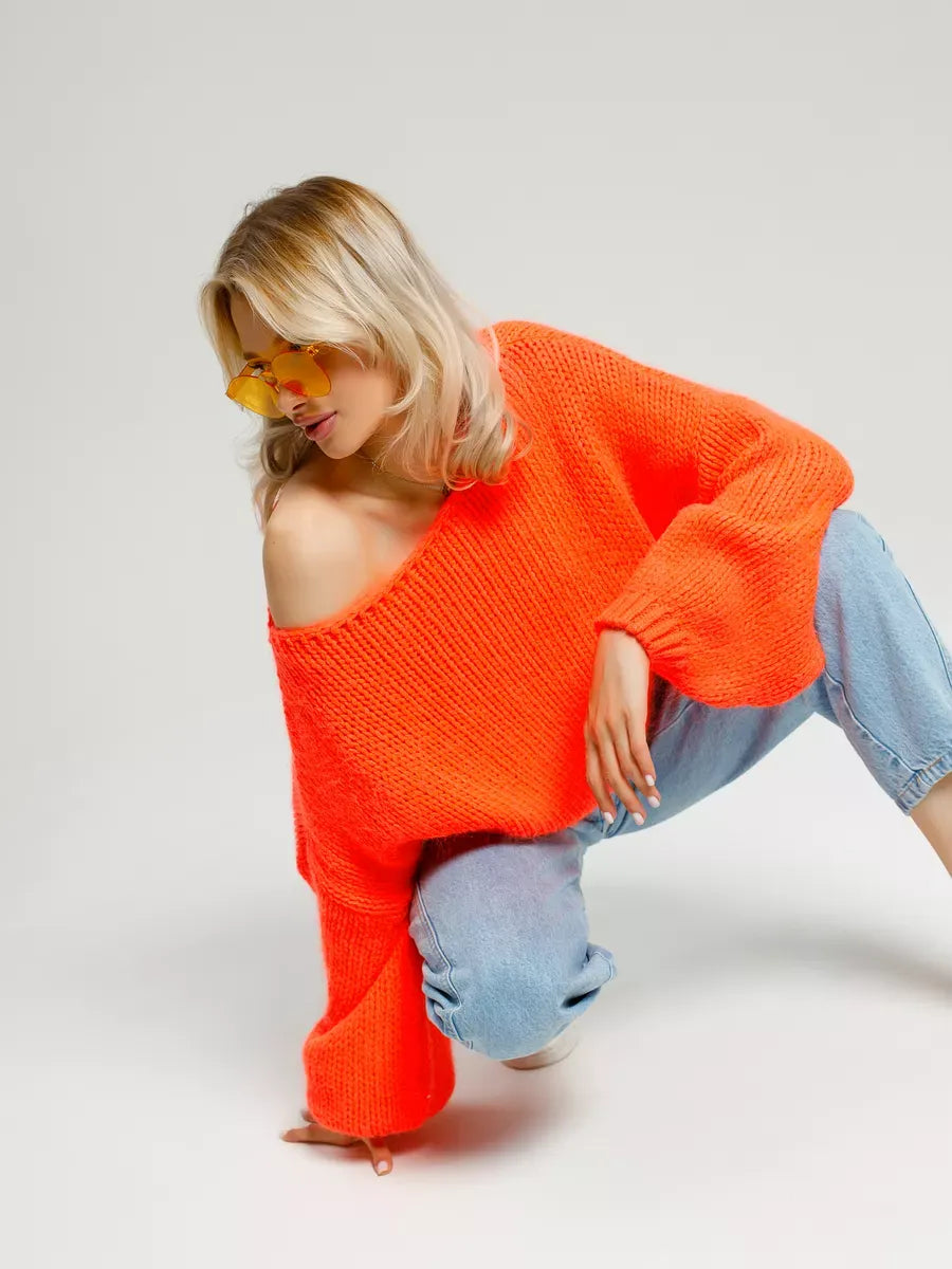 Model wearing the Nova Sweater by Lauven, an oversized off-shoulder knit in vibrant neon orange.