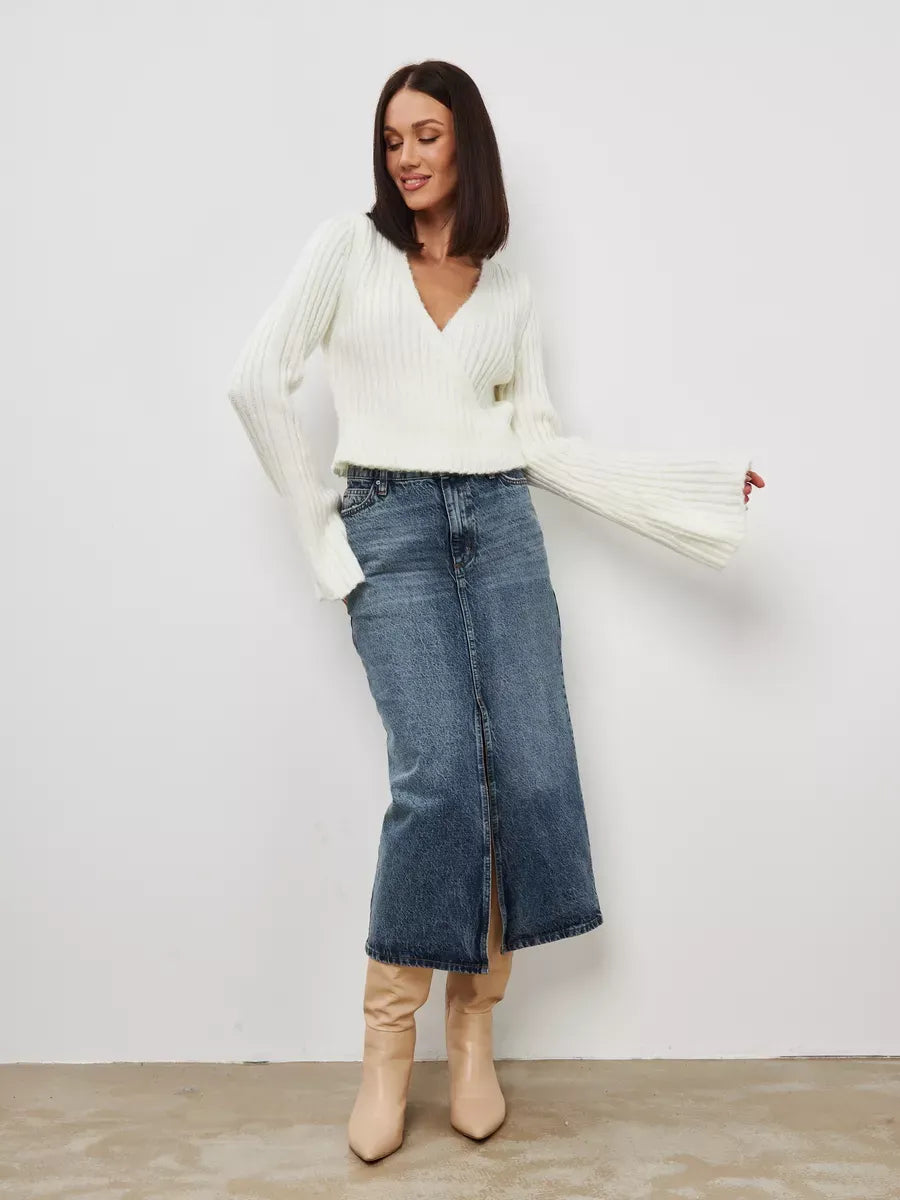 Model wearing the Lyra Sweater by Lauven, a cropped cream knit with a V-neck and wide sleeves, paired with a denim skirt.