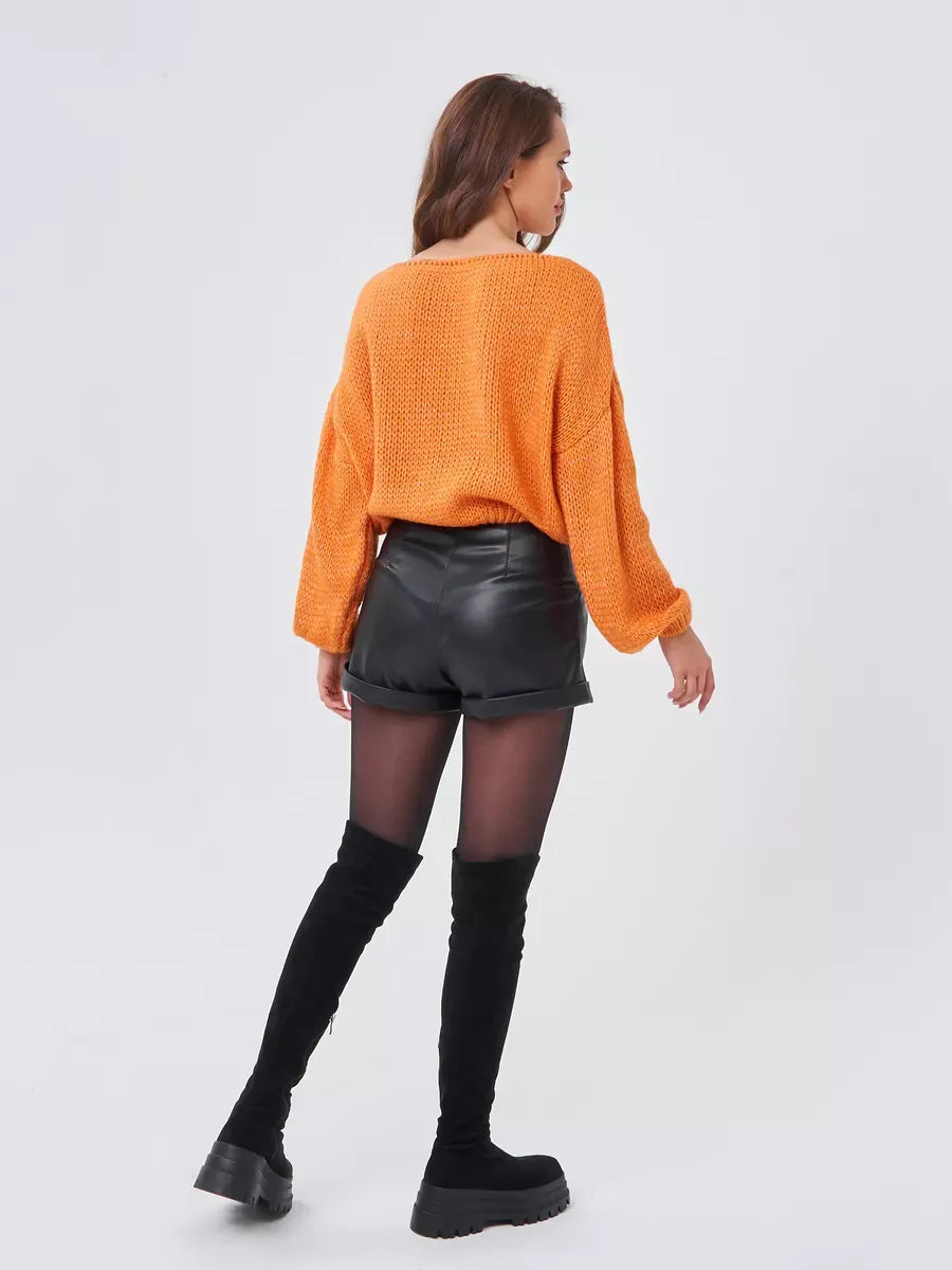 Model wearing Solara Sweater by Lauven in oversized orange knit, paired with black shorts and thigh-high boots.