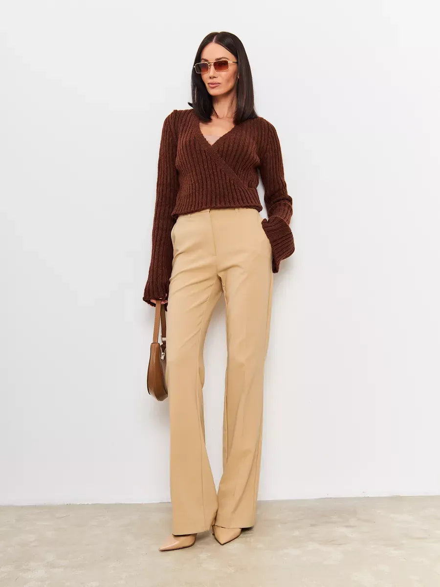 Model wearing Orion Sweater by Lauven, a cropped brown knit with V-neck and wide sleeves paired with beige trousers.