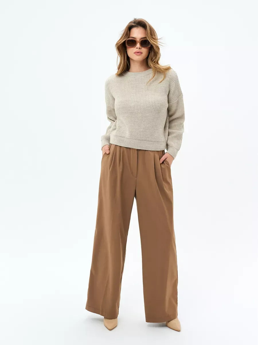A model showcasing the Astra Sweater by Lauven, a light beige oversized knit paired with stylish wide-leg trousers.