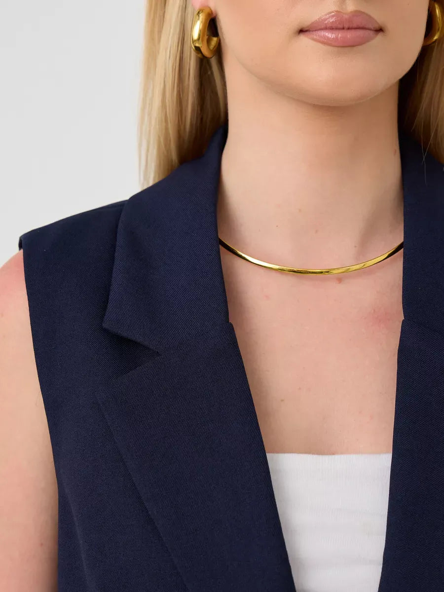 Close-up of a woman wearing the Orion Suit Set by Lauven, featuring a sleeveless navy vest and a statement necklace.