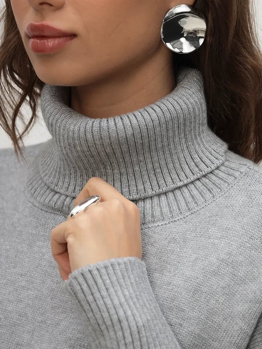 Woman wearing a light grey turtleneck Lyra Sweater by Lauven, showcasing elegant minimalism and cozy sophistication.