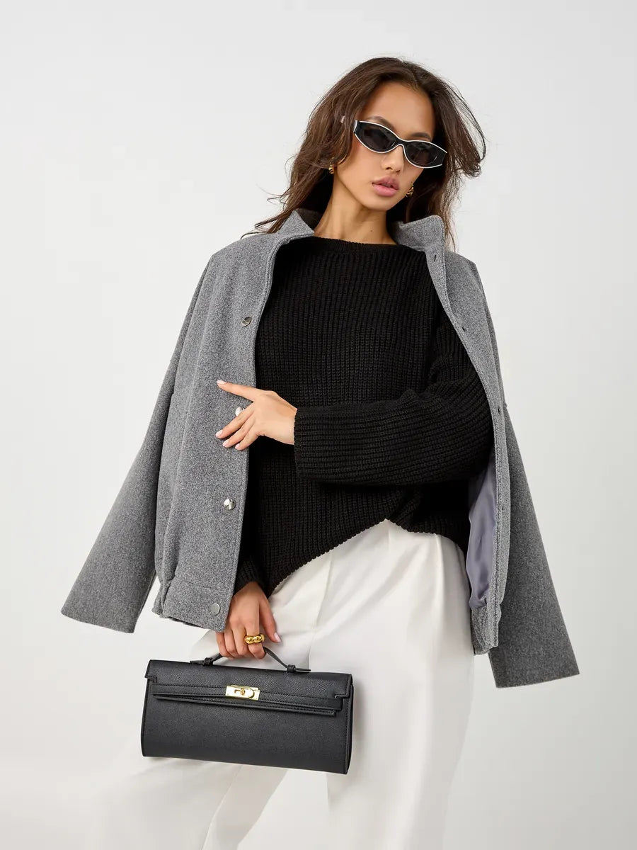 Stylish woman wearing a gray jacket and Nola Sweater, carrying a black handbag with sunglasses.