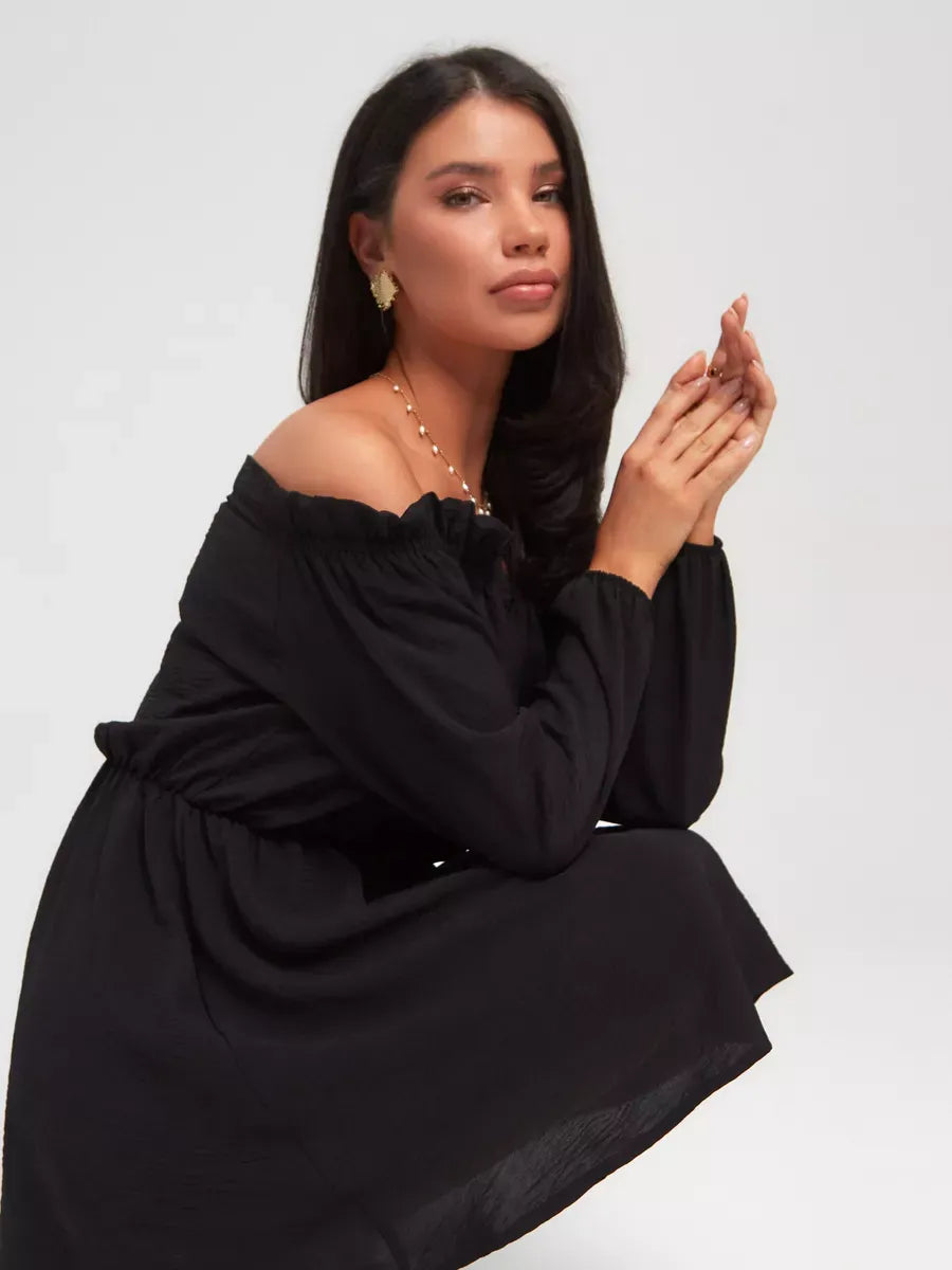 Model showcasing the Nova Mini Dress by Lauven, a classic off-shoulder black mini dress perfect for elegant occasions.