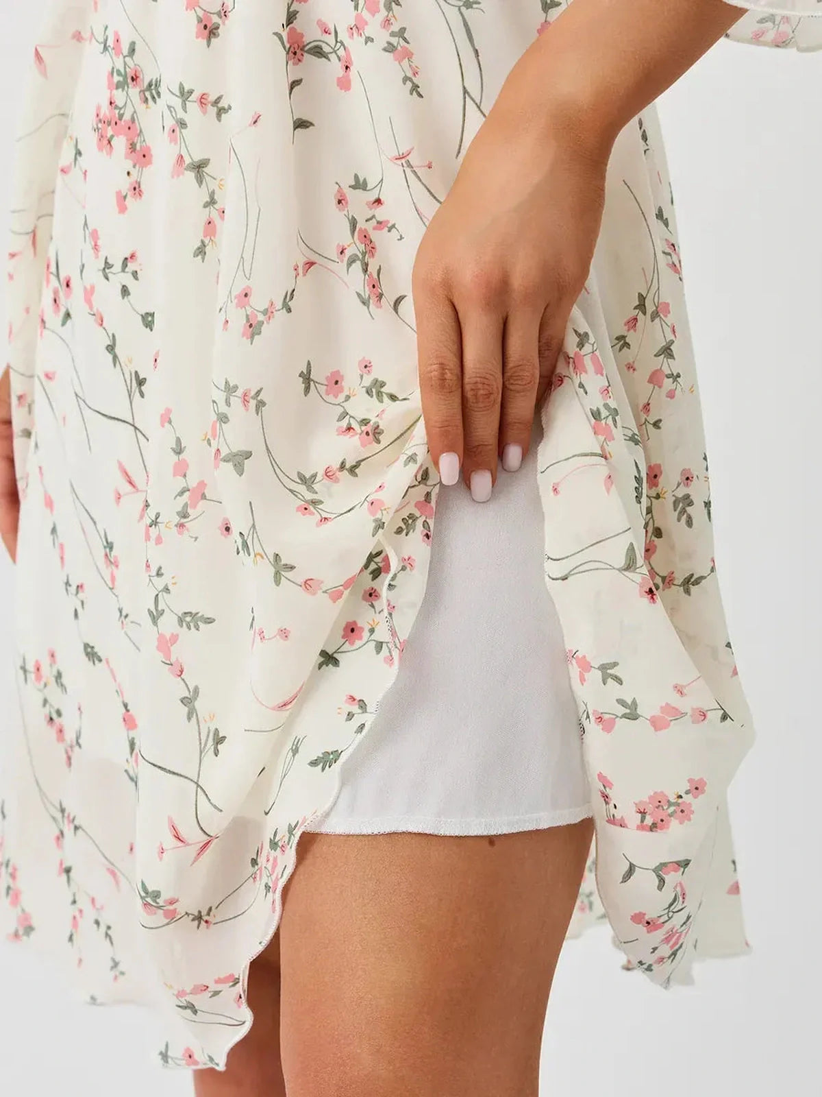 Close-up of hand adjusting the hem of the Petunia Mini Dress by Lauven, featuring a white floral pattern.
