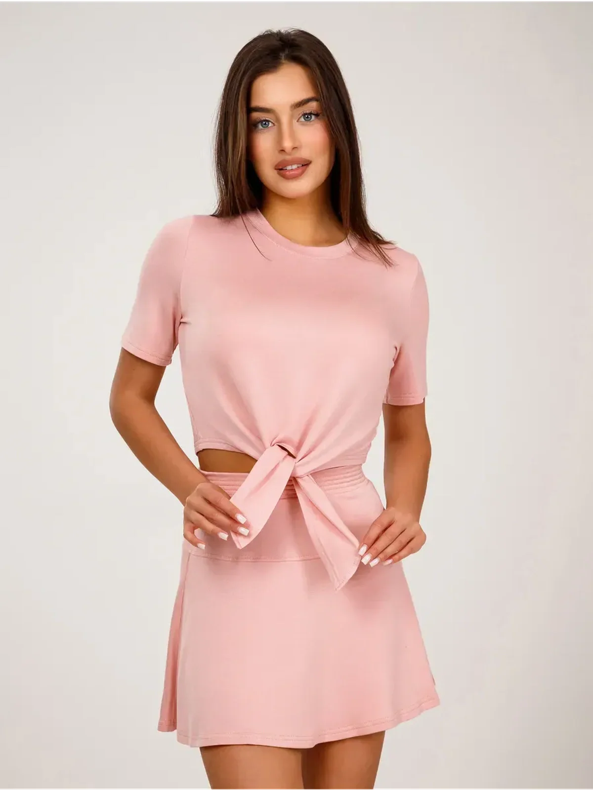 Serena Set by Lauven features a women's two-piece cropped top with tie detail and flared mini skirt in soft pink.