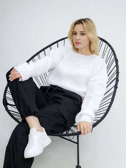 Model wearing Alba Pullover by Lauven, a lightweight knit in soft white, sitting in a stylish chair.