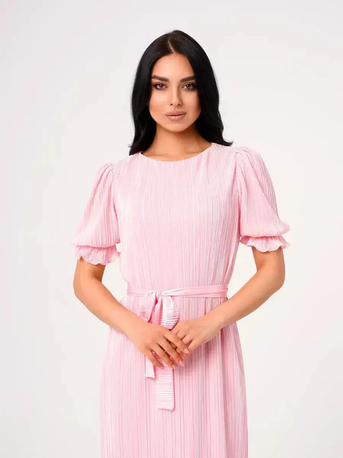 Elegant woman in a pink Candy Maxi Dress with pleated fabric and puff sleeves, featuring a tie waist for a flattering fit.