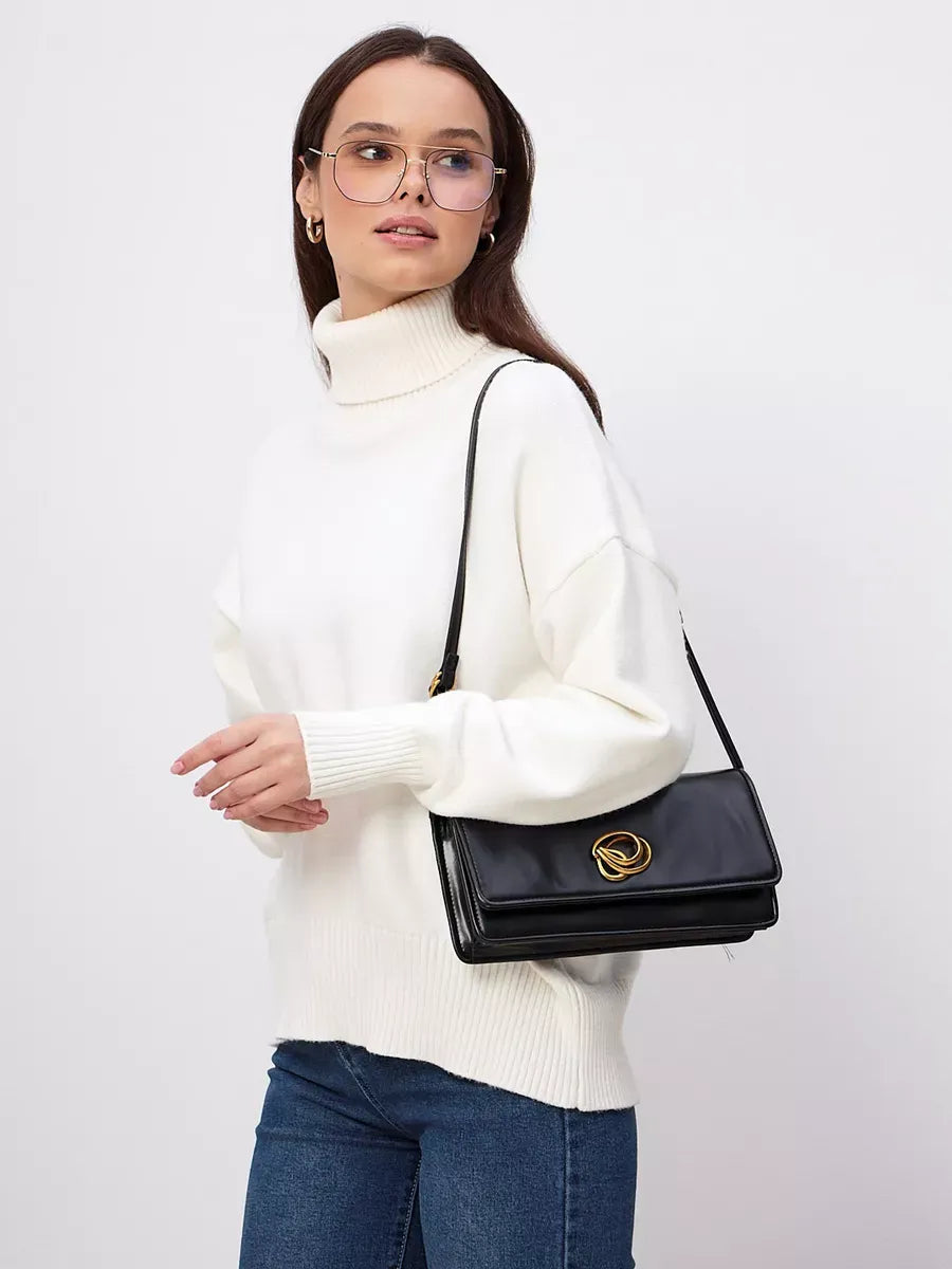 Woman wearing the Elara Sweater with a turtleneck in milk white, accessorized with a stylish black bag.