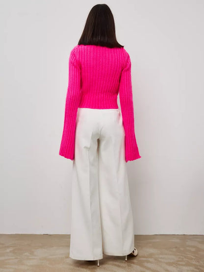 Back view of Selene Sweater by Lauven in bold fuchsia with wide cuffs, styled with white wide-leg pants.