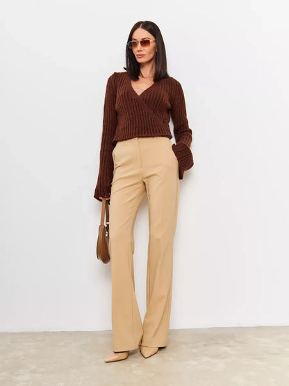 Model wearing Orion Sweater by Lauven, a cropped brown knit with V-neck and wide sleeves paired with beige trousers.