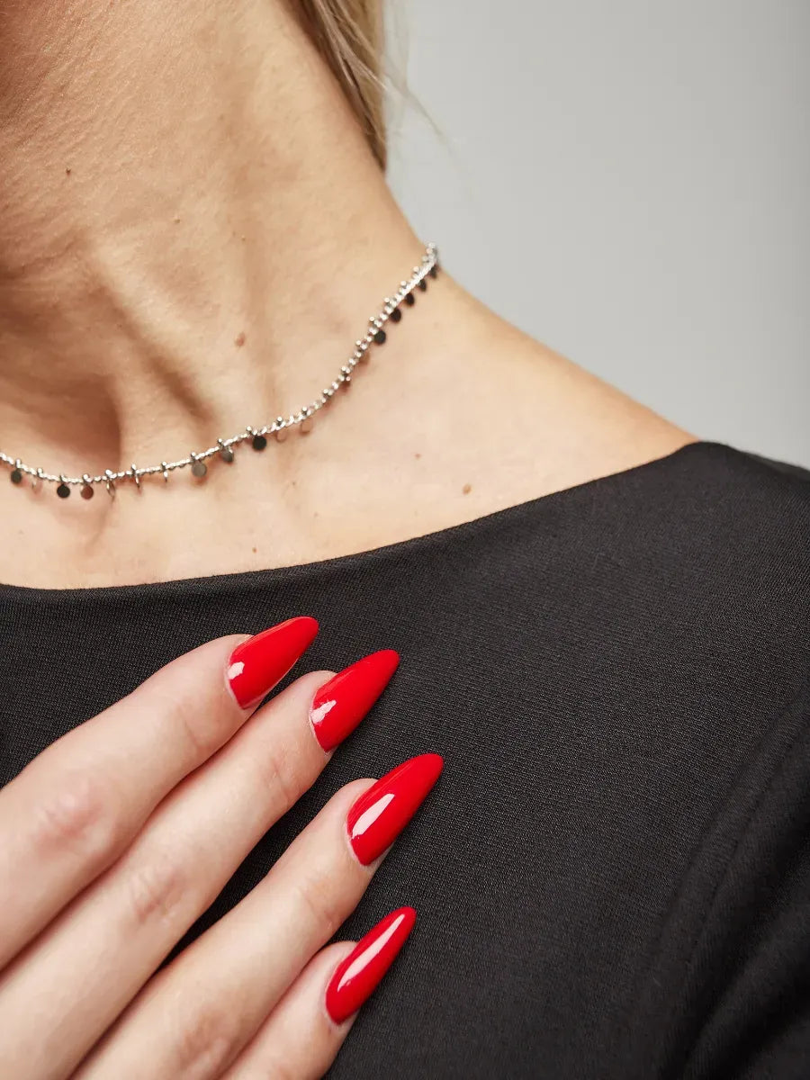 Close-up of a model wearing a silver necklace and red manicured nails, showcasing elegance and style.