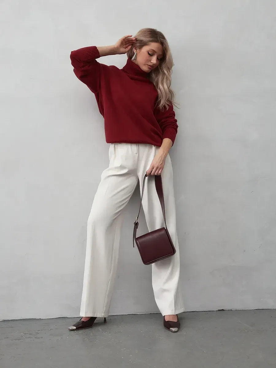 Model wearing Arden Sweater in burgundy with white pants and a burgundy handbag.