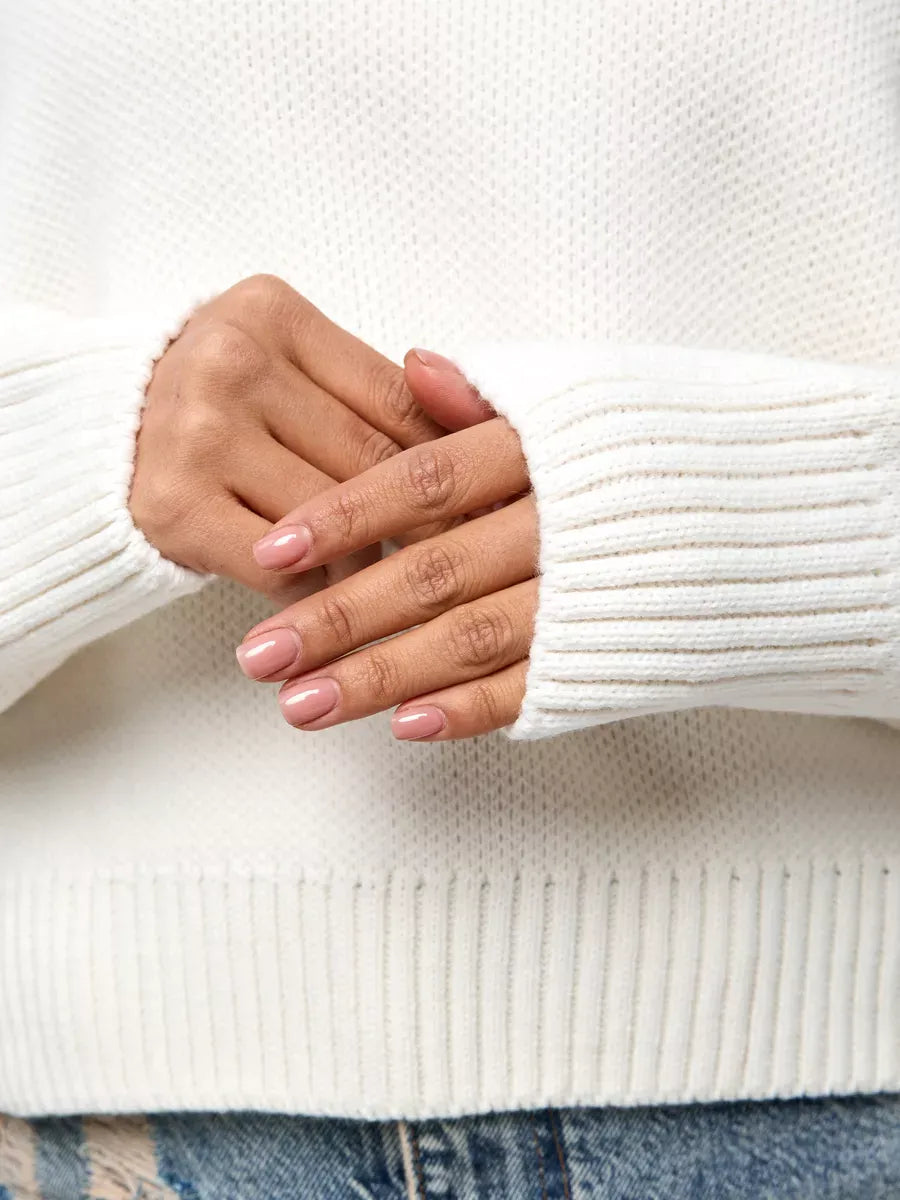 Close-up of hands wearing the Celeste Pullover by Lauven, showcasing the soft ivory knit and ribbed cuffs.
