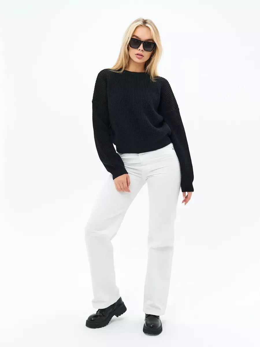 Model wearing Eclipse Sweater by Lauven, an oversized knit in classic black, paired with white pants.
