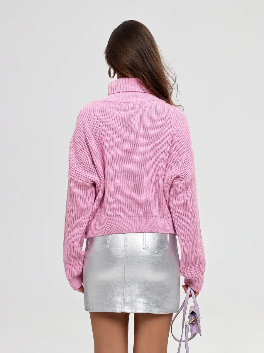 Back view of a woman wearing the Iris Sweater by Lauven, an oversized pink knit turtleneck paired with a silver mini skirt.