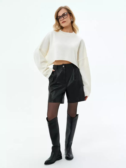 Model wearing the Ivory Sweater by Lauven, cropped oversized knit in white paired with black shorts and knee-high boots.