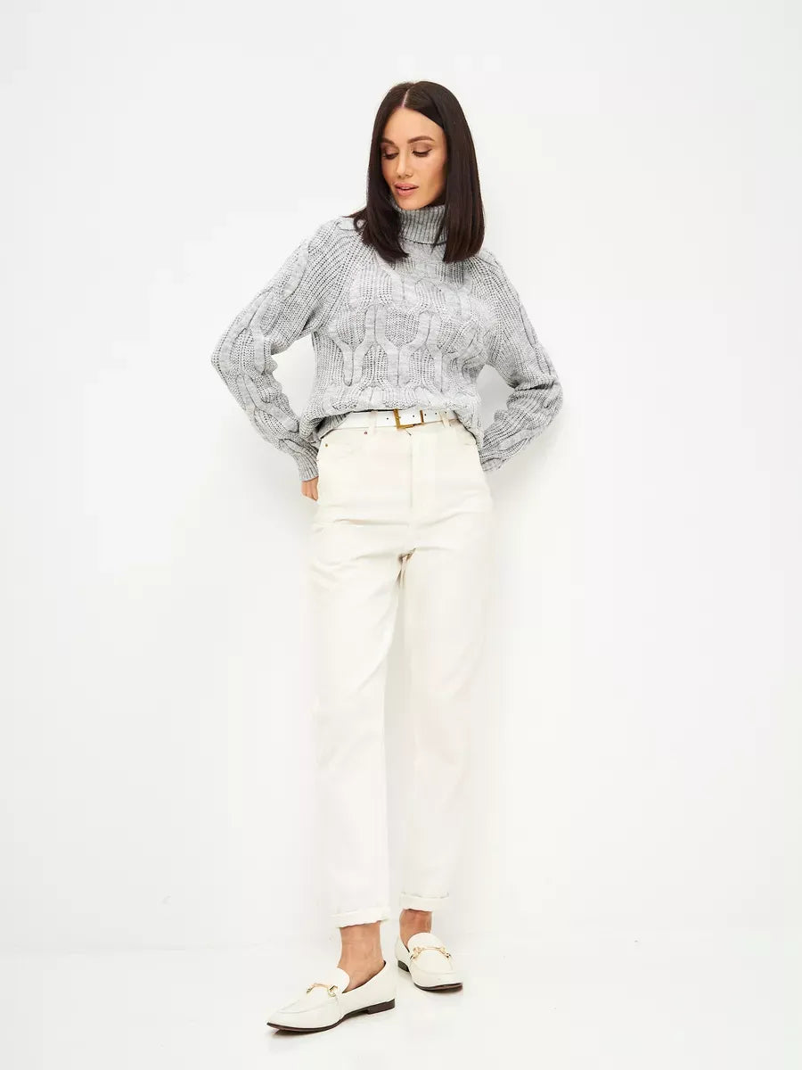 Woman wearing Osiris Sweater by Lauven, oversized cable knit high neck in soft gray melange, paired with white trousers.
