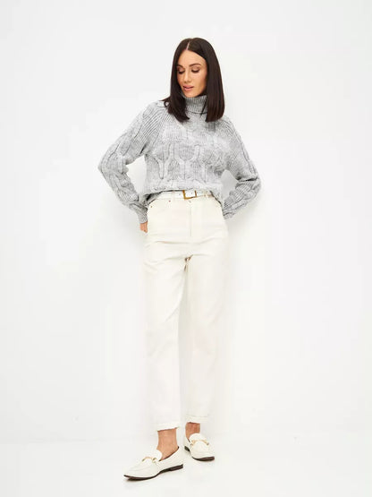 Woman wearing Osiris Sweater by Lauven, oversized cable knit high neck in soft gray melange, paired with white trousers.