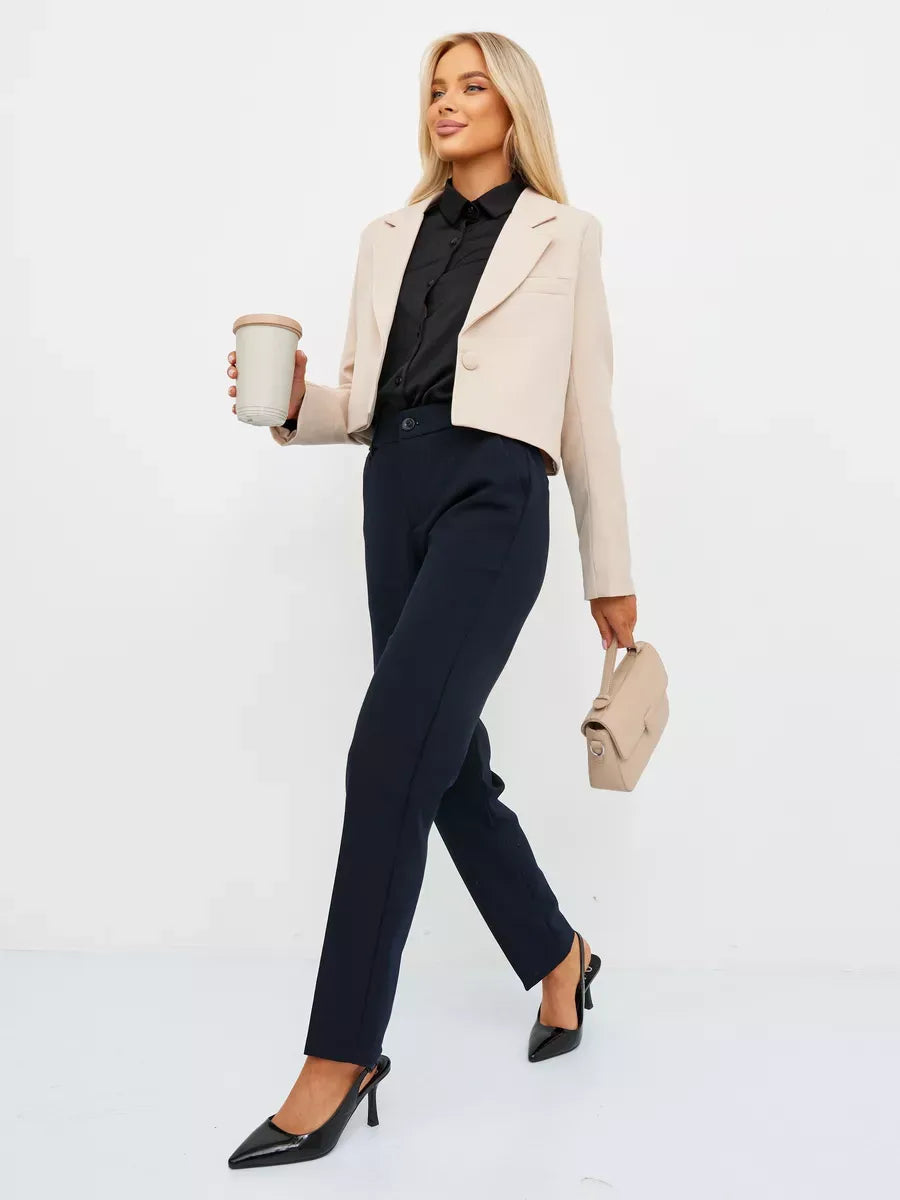 A stylish model wearing a Sandstone Blazer by Lauven, paired with tailored pants and holding a coffee.