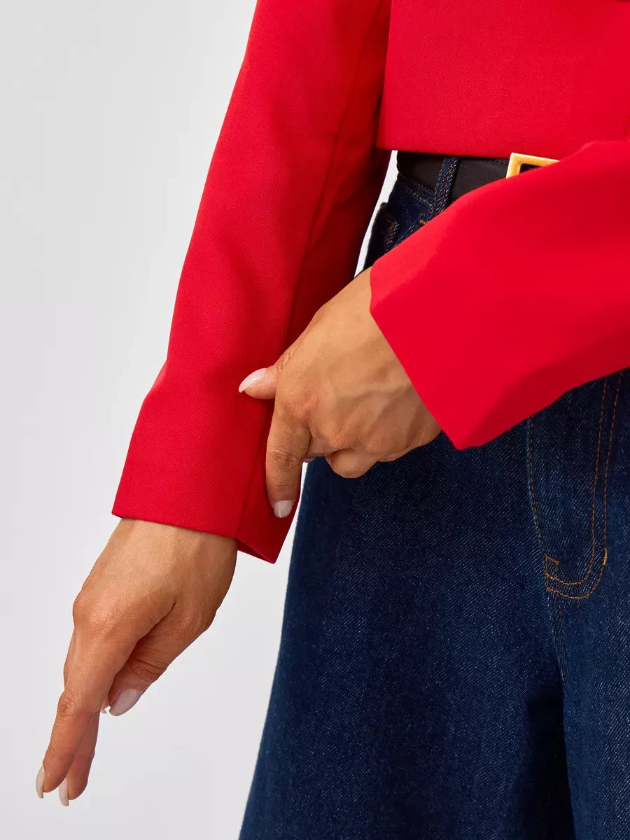 Close-up of a hand adjusting the sleeve of the Ruby Blazer by Lauven, showcasing its vibrant red color and tailored design.