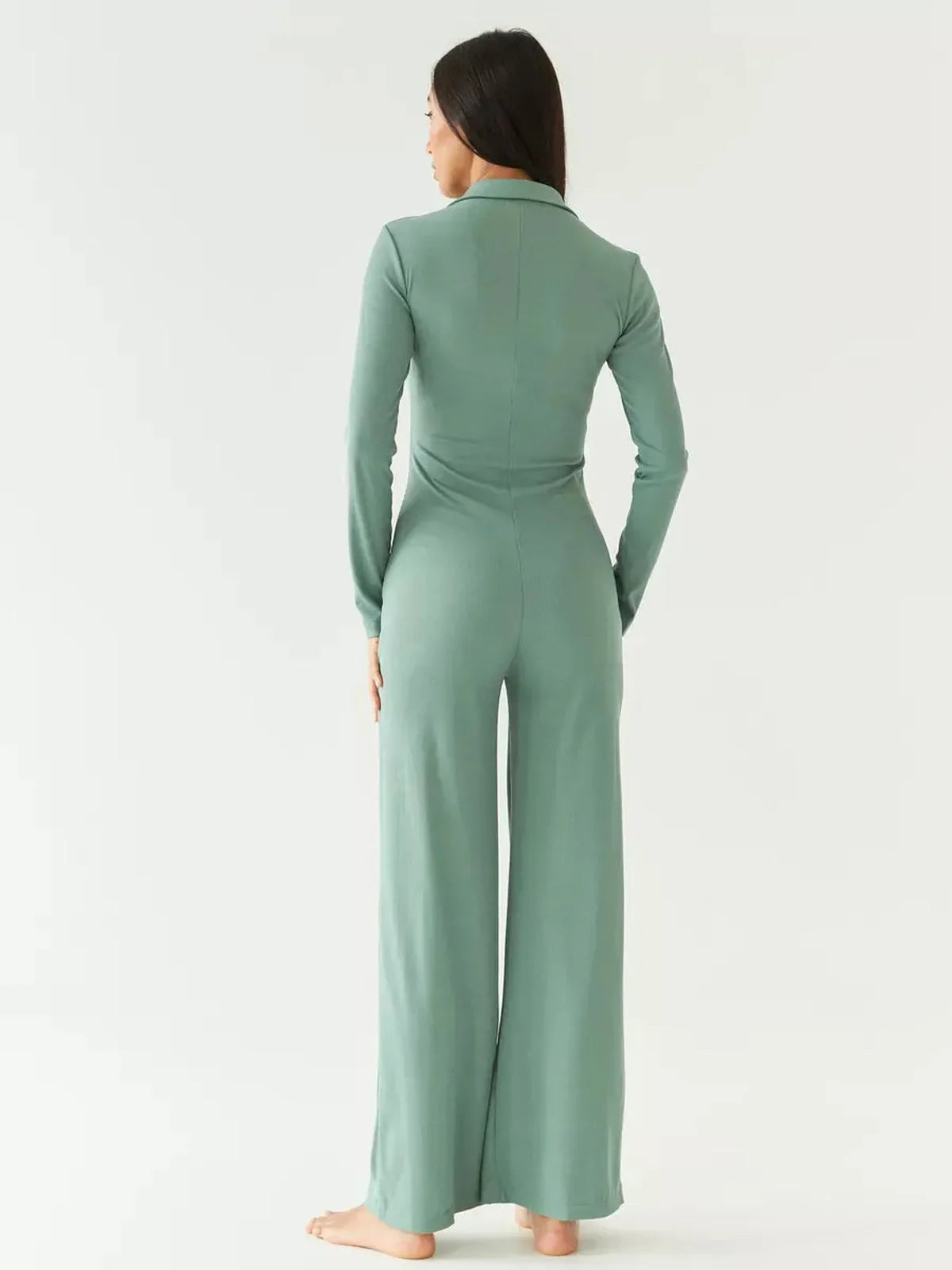 Model showcasing the back view of the Scarlett Jumpsuit in sage green with wide-leg silhouette and structured collar.