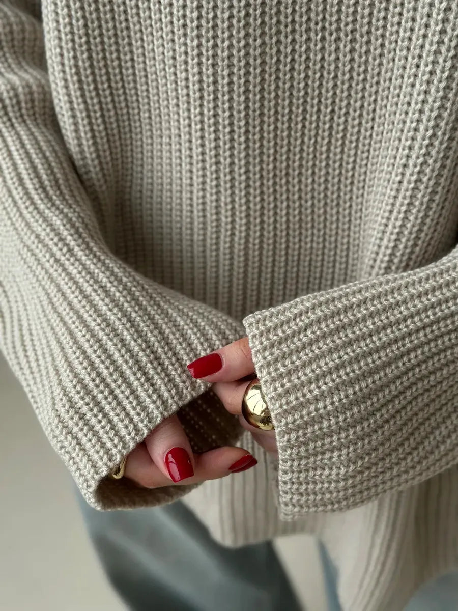 Close-up of hands wearing the Sierra Sweater by Lauven, showcasing its oversized beige knit and relaxed fit.