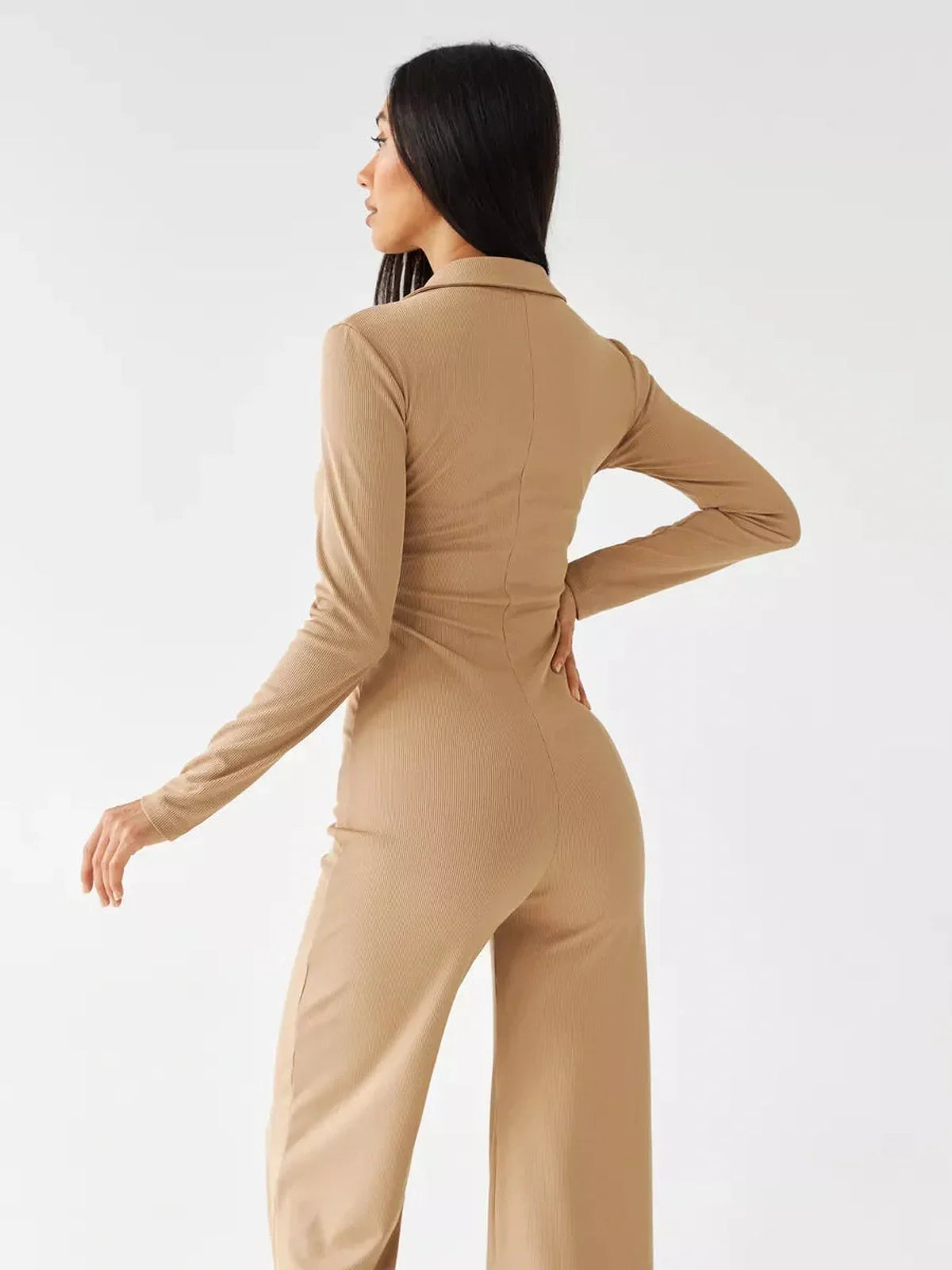 Jersey Jumpsuit showcasing a woman in a sand ribbed knit fabric with a button-front and wide-leg silhouette from the back.