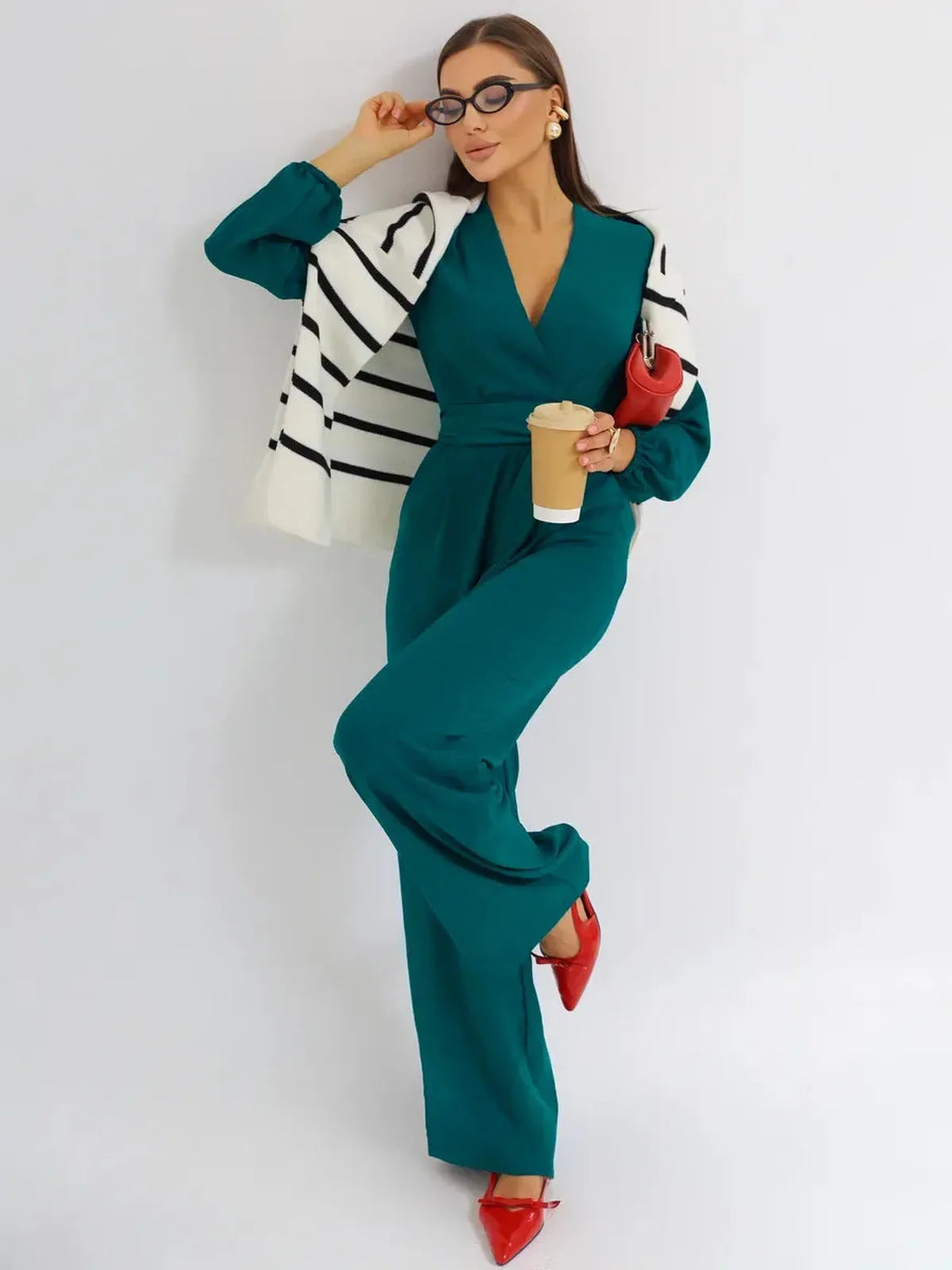 Zoe Jumpsuit in teal with wide-leg trousers, deep V-neckline, styled with a striped shawl and red accessories.