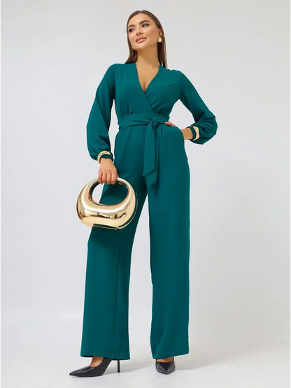 Zoe Jumpsuit in green featuring wide-leg trousers, deep V-neckline, and self-tie belt, styled with a gold handbag.