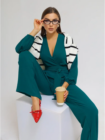 Zoe Jumpsuit modeled by a woman with glasses, featuring wide-leg trousers, a wrap-effect bodice, and a self-tie belt.