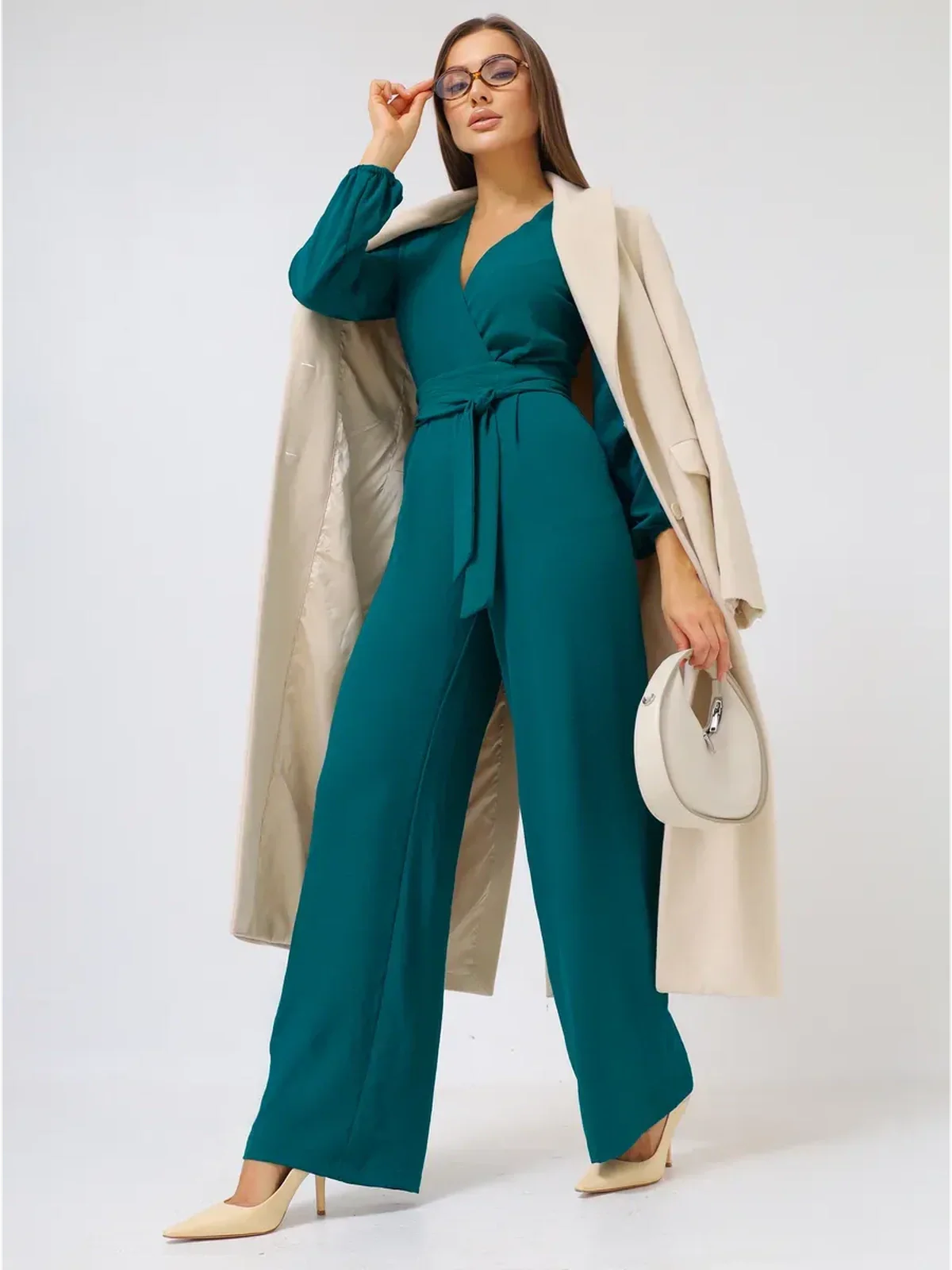 Zoe Jumpsuit in teal with wide-leg trousers and a self-tie belt, paired with a light coat and handbag.