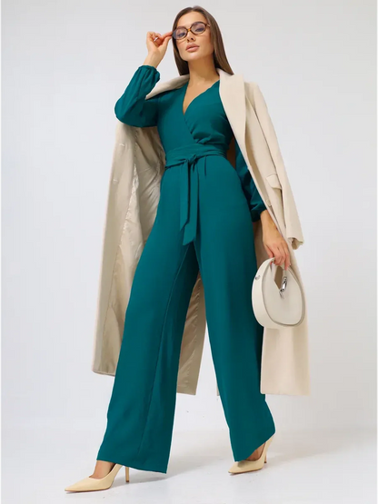 Zoe Jumpsuit in teal with wide-leg trousers and a self-tie belt, paired with a light coat and handbag.