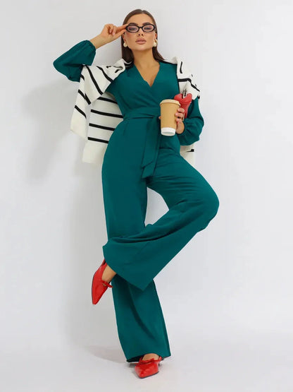 Model wearing Zoe Jumpsuit in teal with wide-leg trousers and self-tie belt, styled with a striped jacket.
