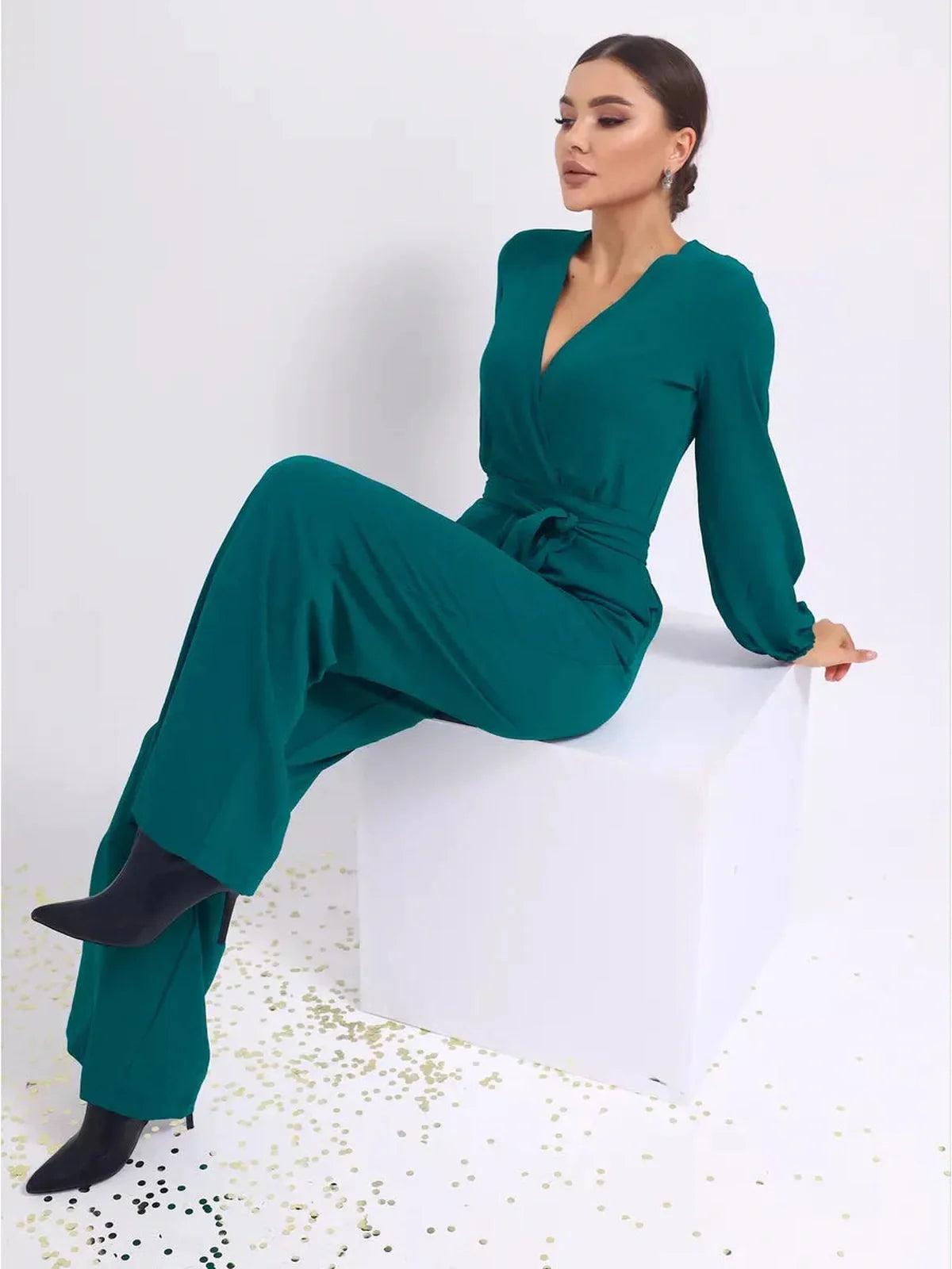 Zoe Jumpsuit in teal color with a deep V-neckline, wide-leg trousers, and belted design, styled with heels.