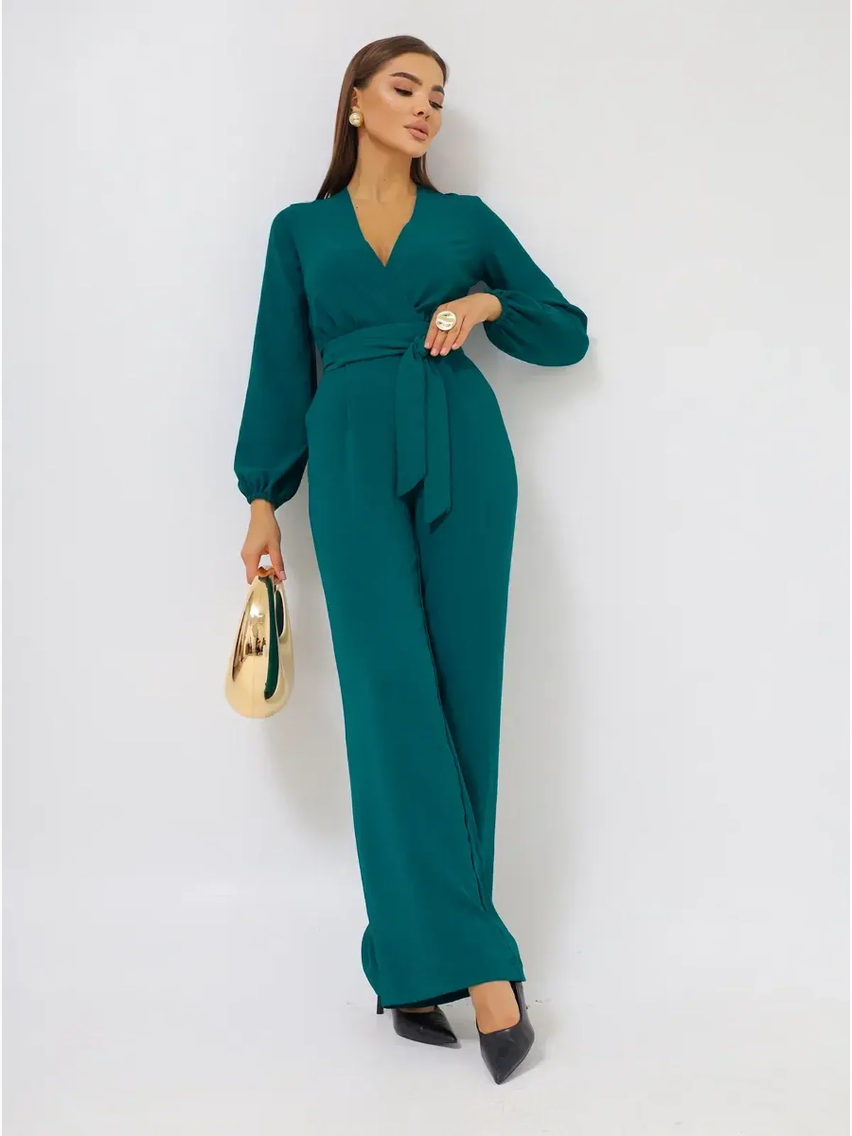 Zoe Jumpsuit in teal featuring a deep V-neckline, wide-leg trousers, and a self-tie belt, styled with a chic handbag.